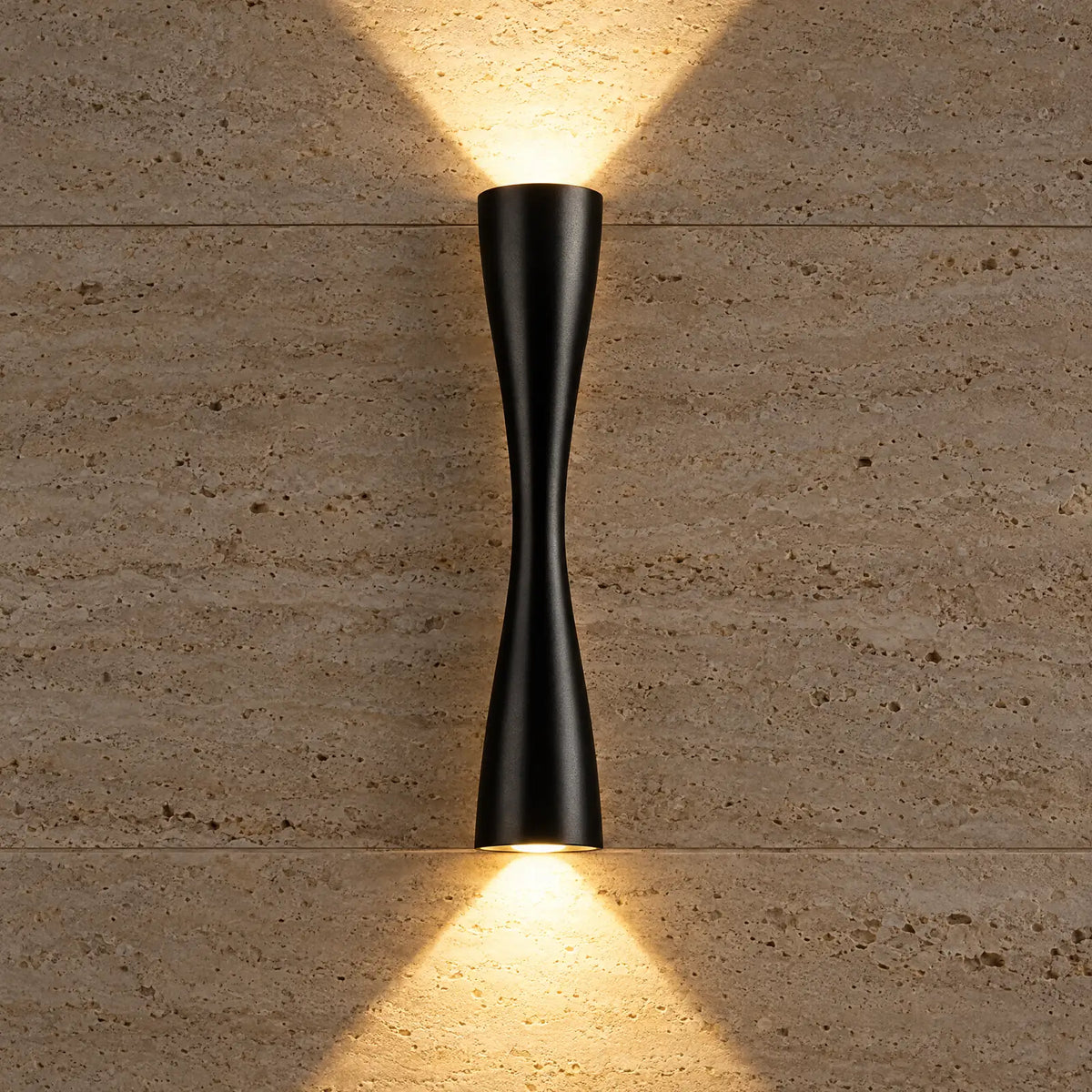 Faisceaux lumineux haut et bas de l'applique Caria noire sur un mur en travertin