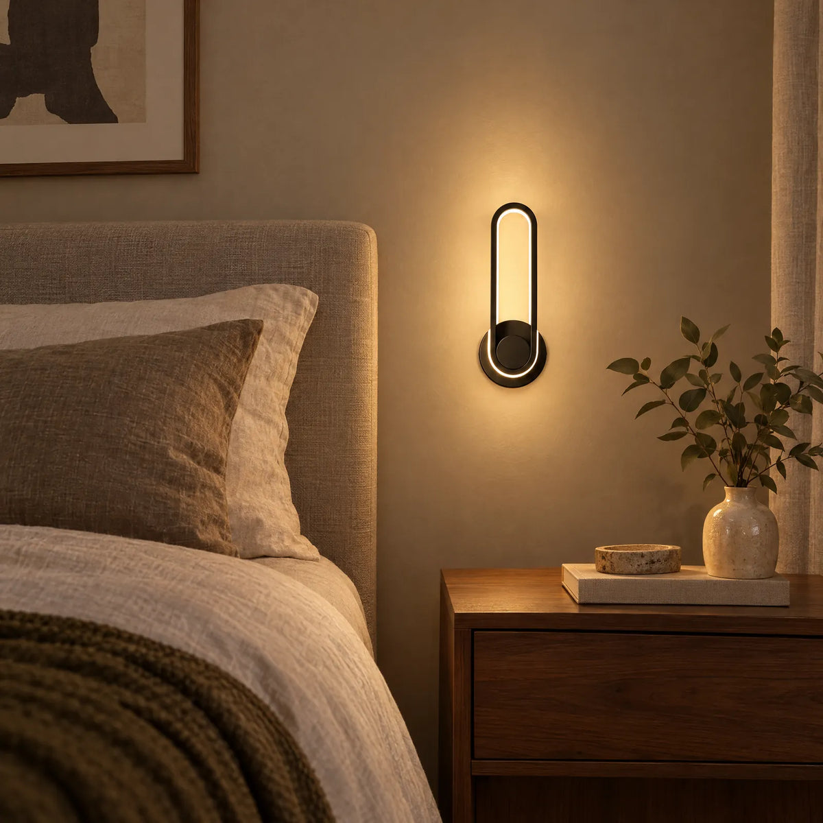 Applique LED Lucio noire allumée à côté d'un lit
