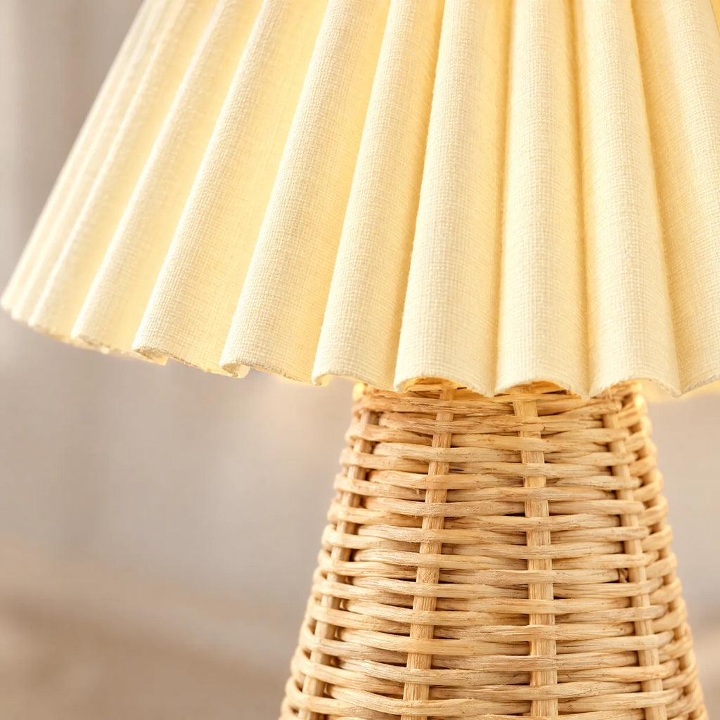 Détail de l'abat-jour plissé allumé et du pied en rotin de la lampe Folia
