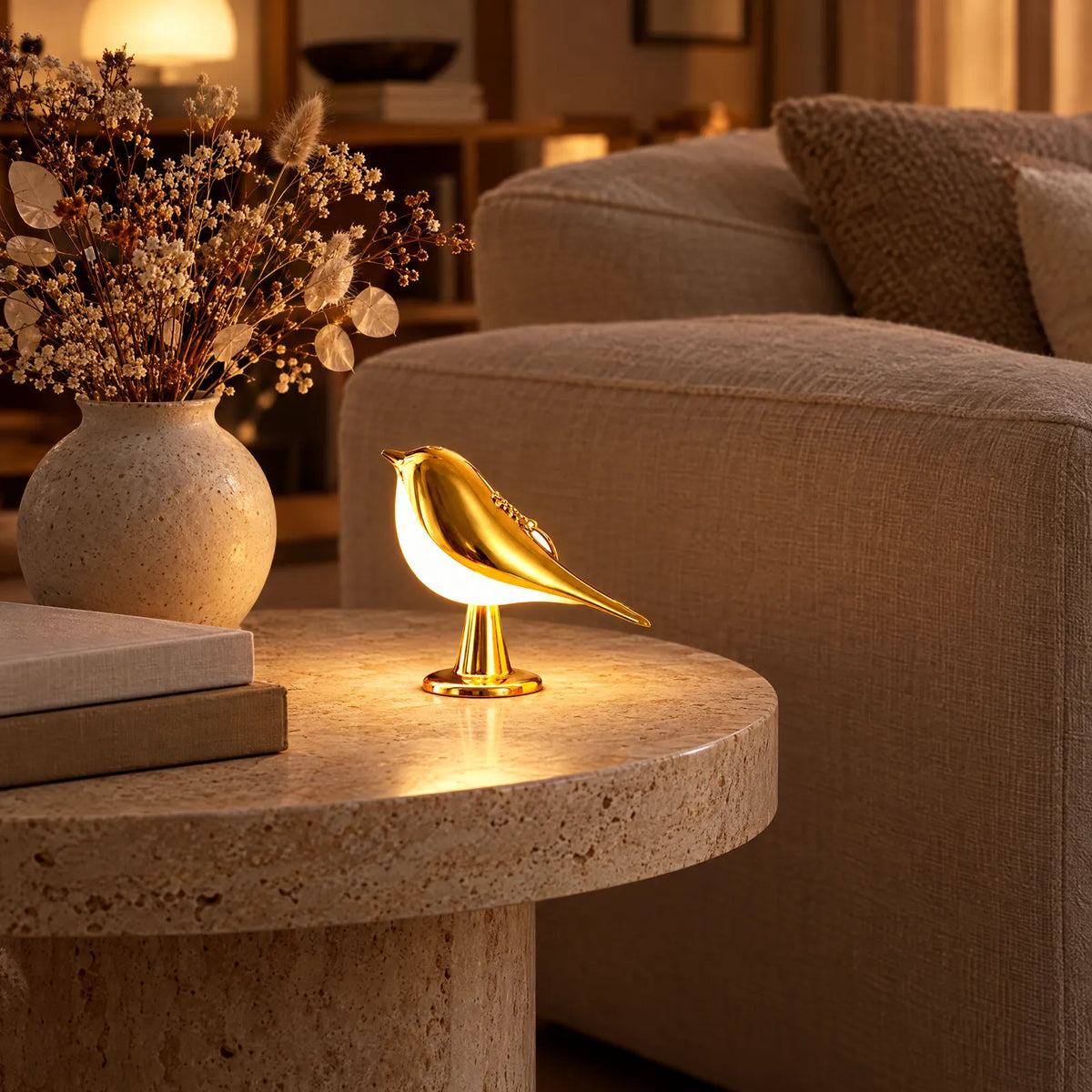 Lampe oiseau Claris dorée allumée sur une table d'appoint en travertin Image