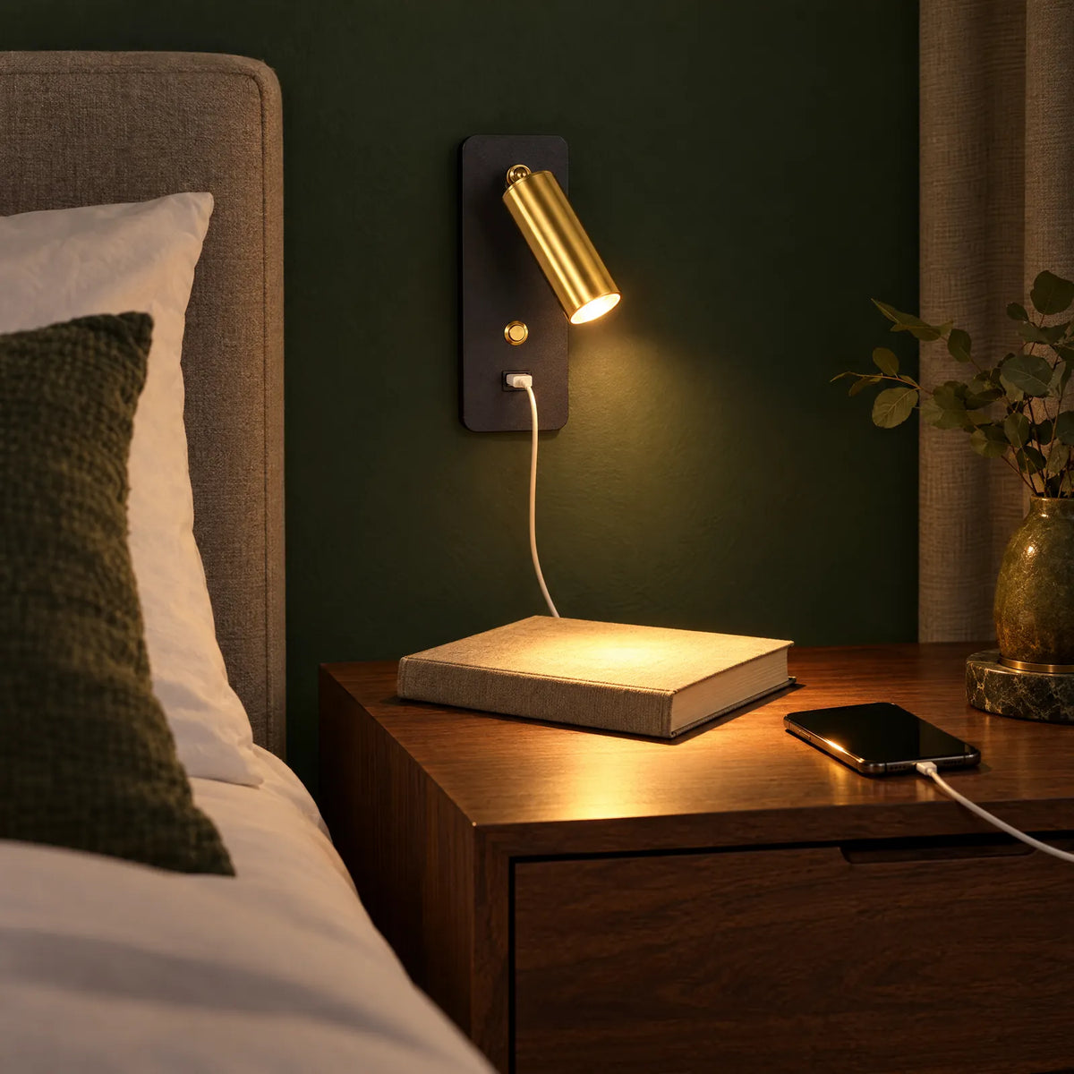 Lampe de chevet murale Alex dorée allumée, téléphone en charge sur la table de nuit Image