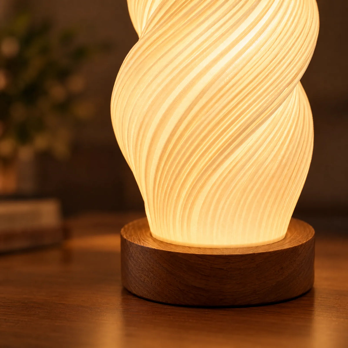 Détail de l'abat-jour torsadé strié allumé et du socle en noyer de la lampe Yva
