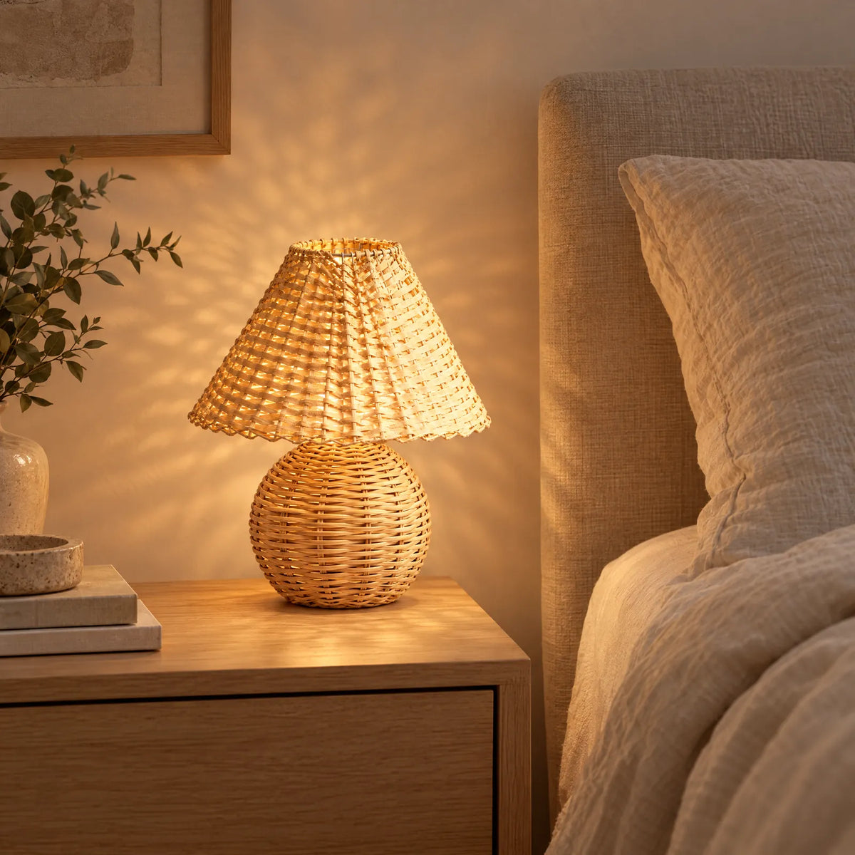 Lampe en bambou Julio allumée sur une table de chevet, reflets du tressage au mur
