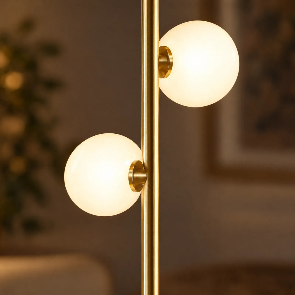Détail des globes en verre opalin allumés et de la tige dorée du lampadaire Polia